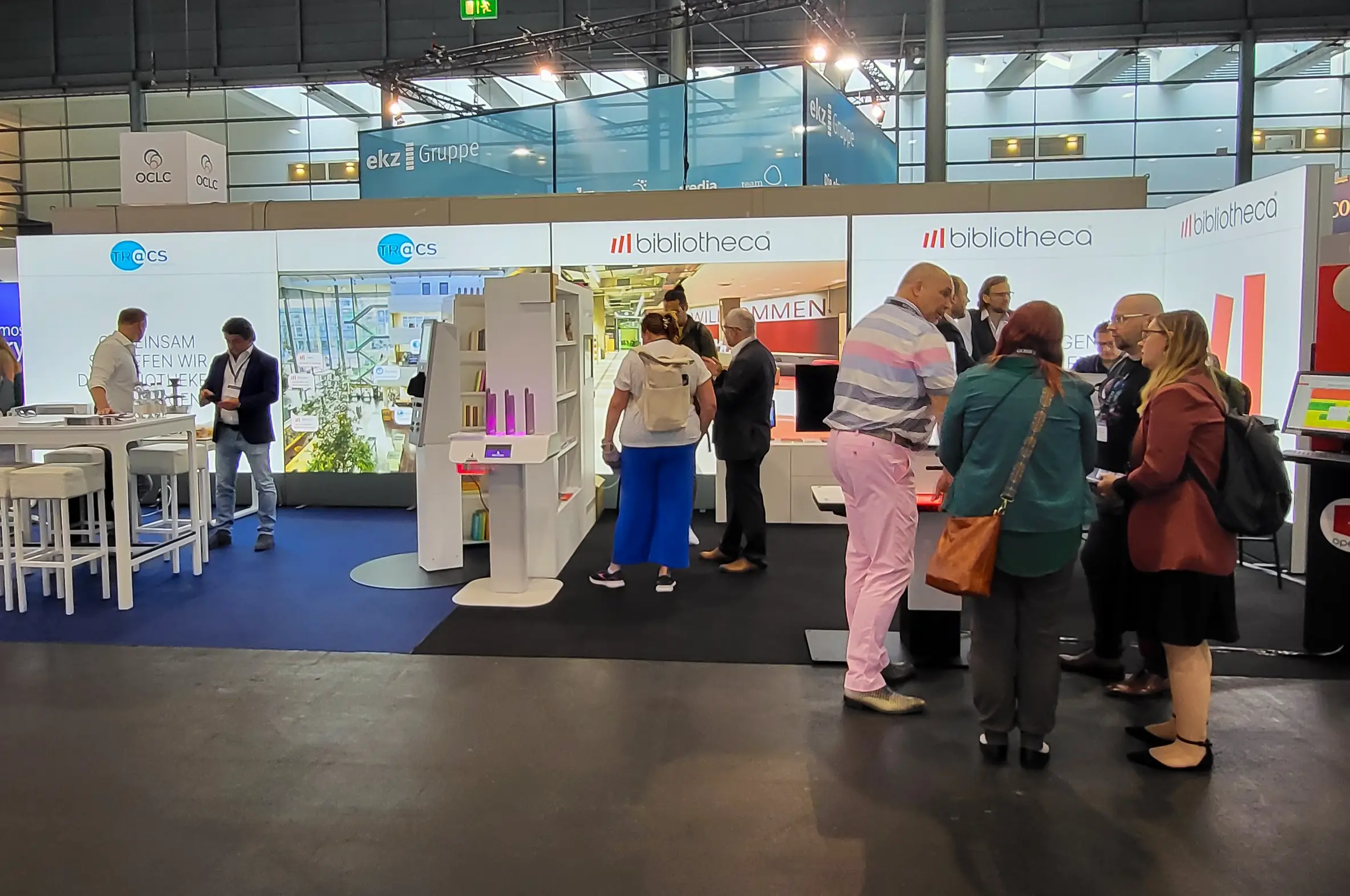Messestand mit mehreren Personen, die sich in einer Gruppe unterhalten, umgeben von Informationsmaterialien.