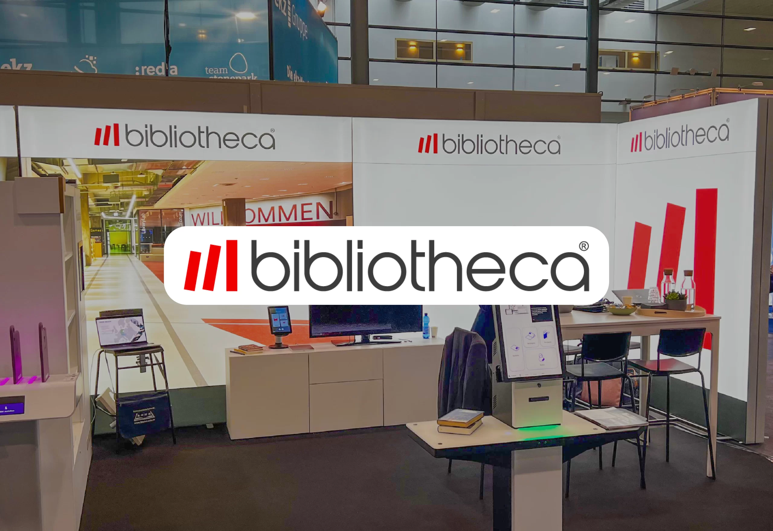 Innenansicht einer modernen Bibliothek mit Empfangstresen und Willkommensschriftzug an der Wand.