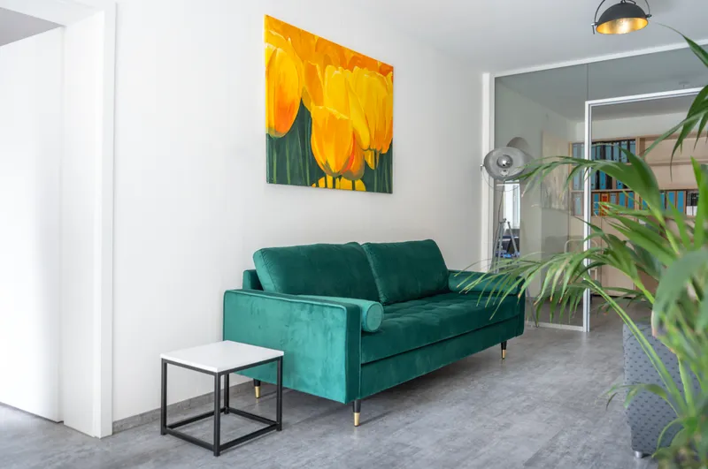 Heller, moderner Loungebereich der heinmedia Kreativagentur mit grünem Samtsofa, gelbem Tulpenbild und Zimmerpflanze.