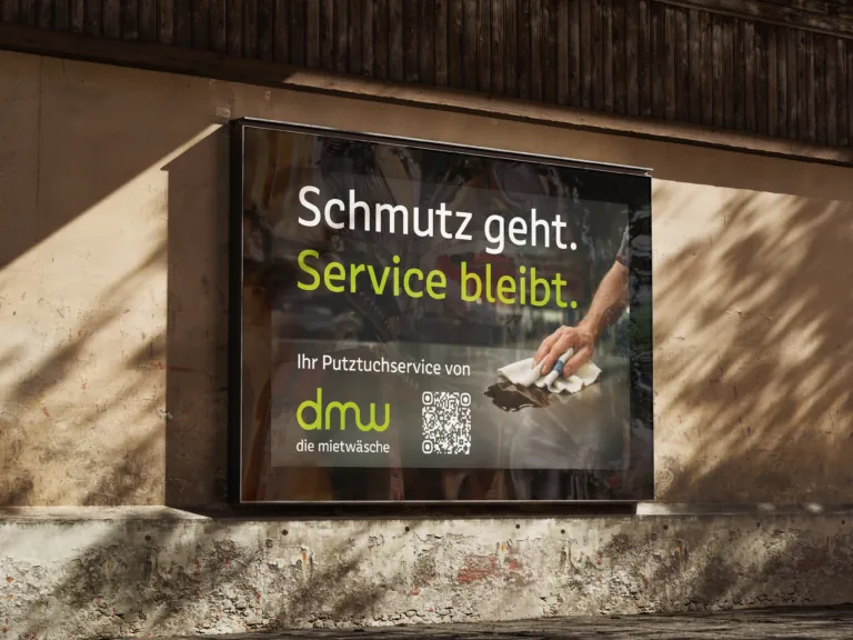 Rückbeleuchtetes Werbebanner an der Wand mit dem Satz 'Schmutz geht. Service bleibt.', DMU Logo und Hand, die ein Tuch verwendet, QR-Code sichtbar