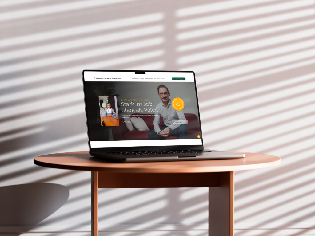 Laptop auf einem Tisch mit einer geöffneten Webseite, die einen Mann zeigt, der auf einem Sofa sitzt.