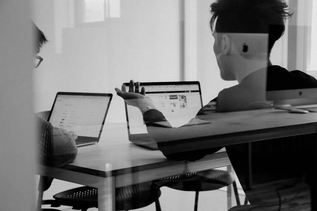 Zwei Personen, die an Laptops arbeiten und sich in einem modernen Büro austauschen.