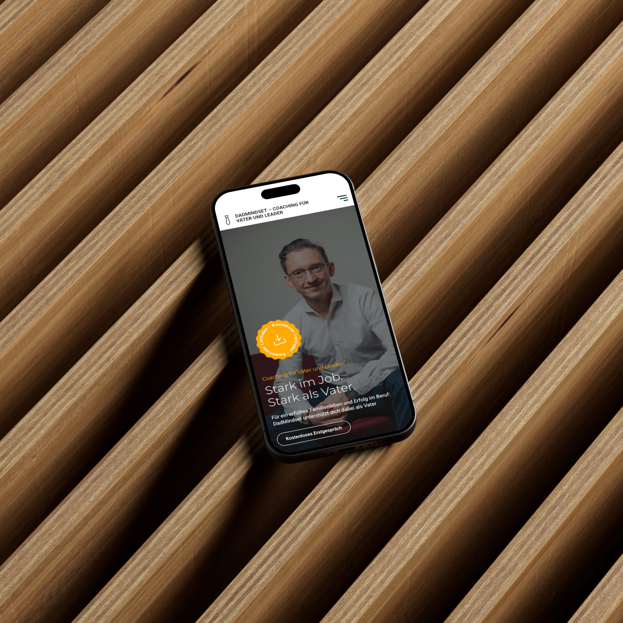 Ein iPhone-Mockup zeigt eine Webseite mit einem Portrait und Text auf einem Holzuntergrund.