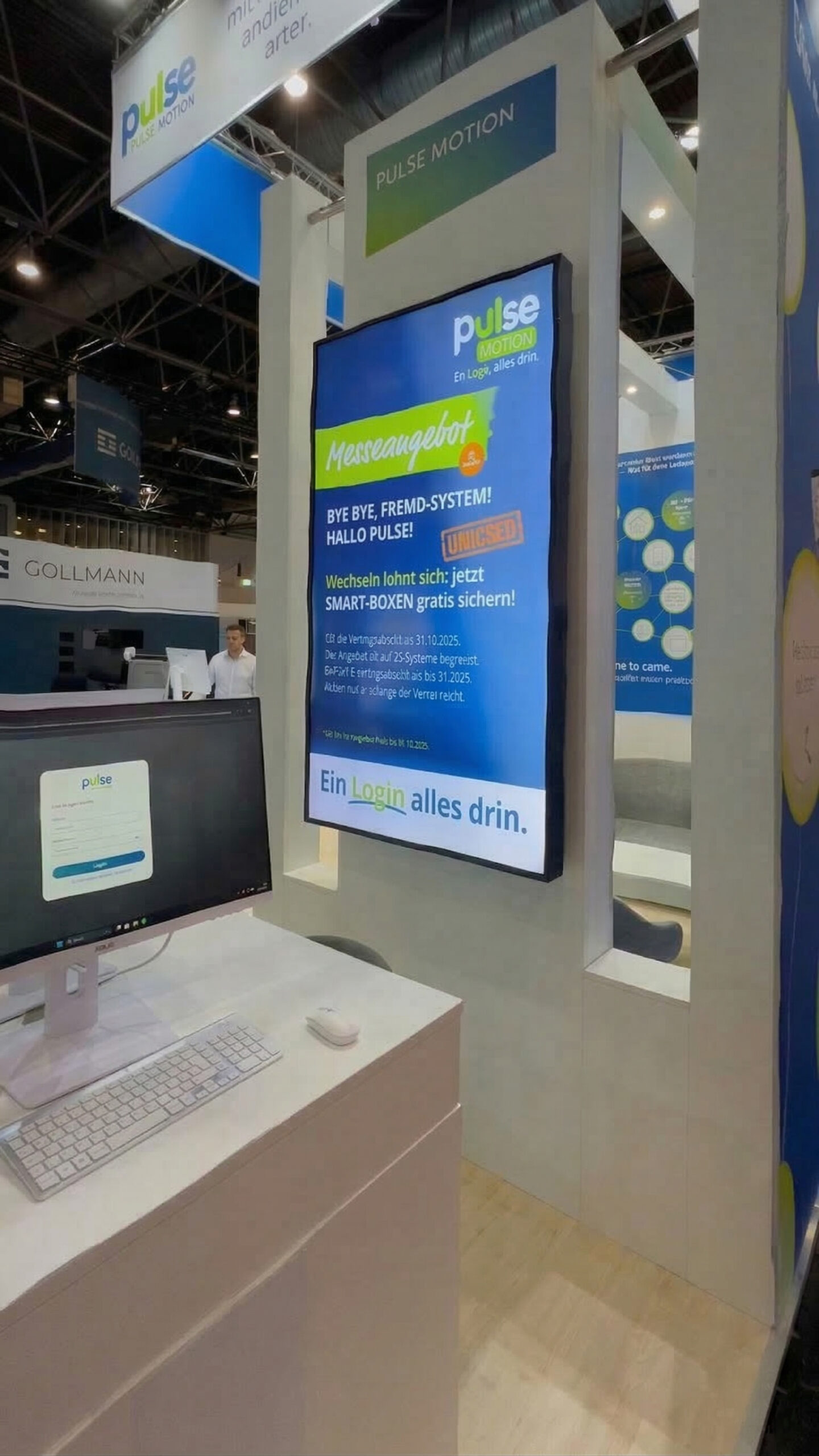 Messestand mit großem digitalen Display von Pulse Motion, weiße Booth-Konstruktion, Computer-Arbeitsplatz und Banner, Messe-Ambiente mit weiteren Ständen im Hintergrund