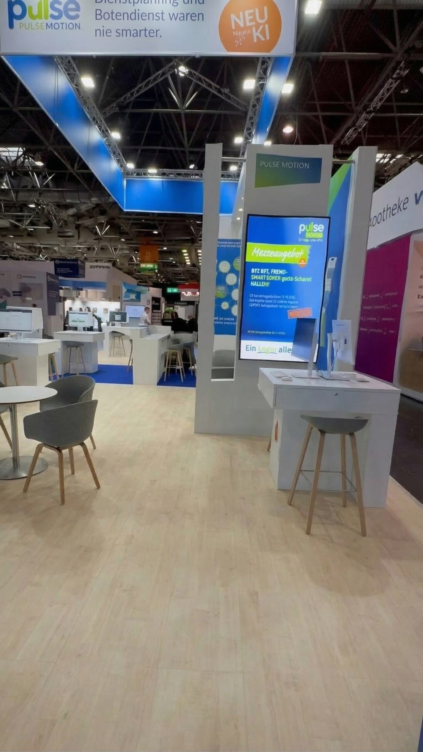 Messestand mit moderner Präsentationswand von Pulse Motion, hellen Holzboden, hellblauen Akzenten, einem digitalen Display und Sitzgelegenheiten aus Stühlen und Hockern.
