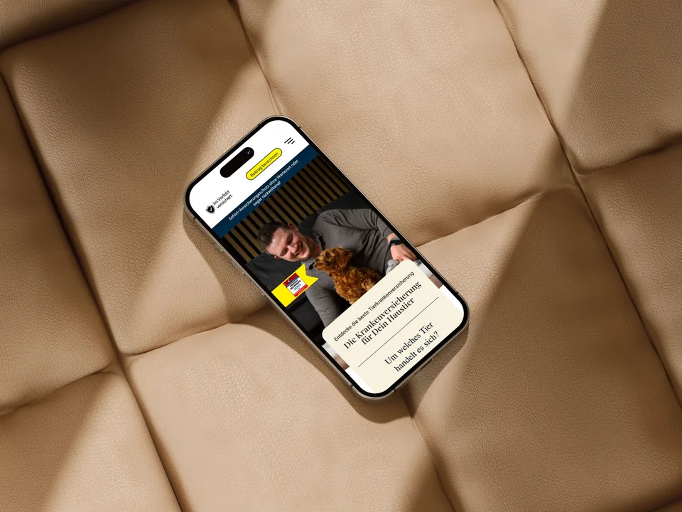 Smartphone auf einem beigen Lederpolster mit dem Einstieg von Im Vorfeld versichert: Foto mit Mann und Welpen, Headline und die erste Frage des Funnels in einer Karte.